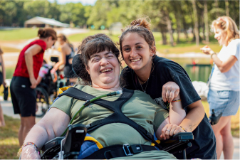 Camp counselor smiling next to a camper in a wheelchair