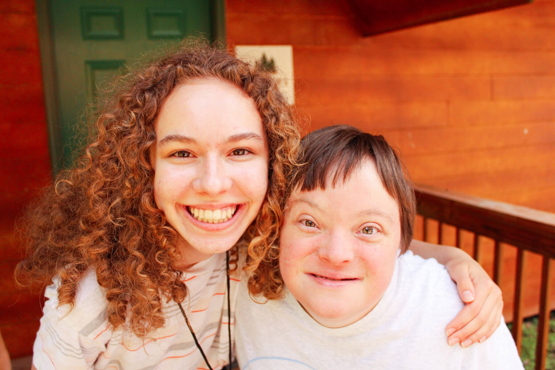 Camper and camp counselor smiling at the camera on a porch