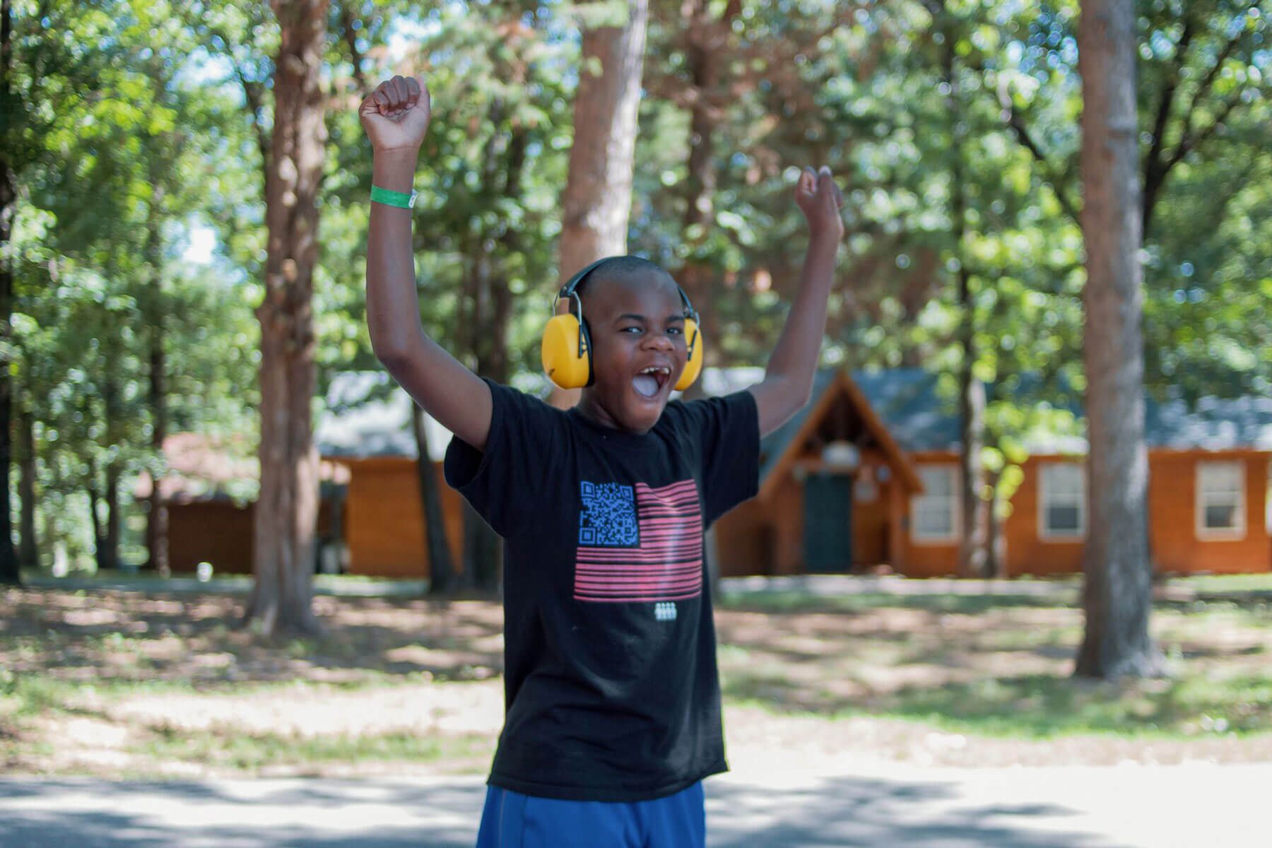 Camper walking with headphones and raised arms smiling and cheering