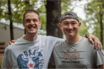 Summer camper and counselor smiling with trees in the background