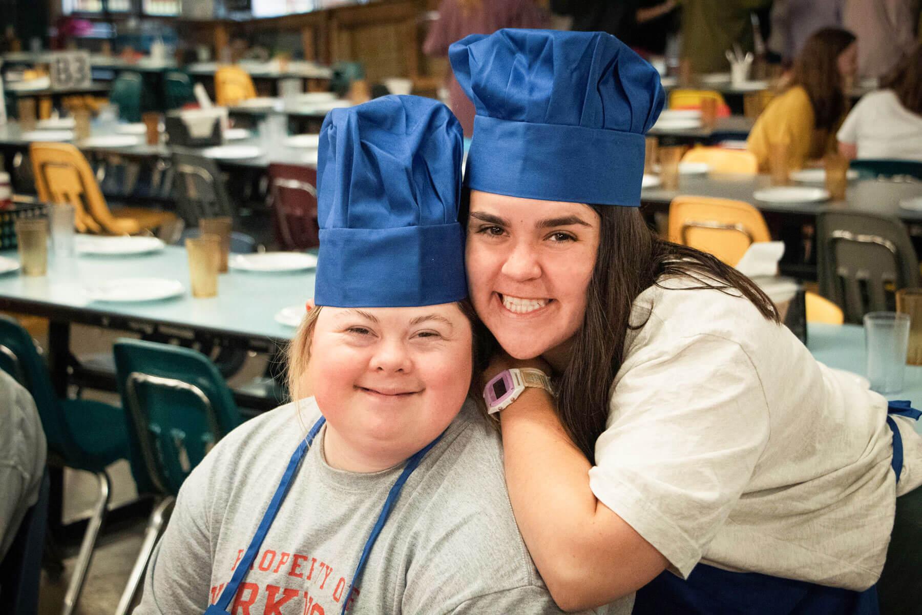 Summer camper with counselor wearing blue chef's hats in a cafeteria