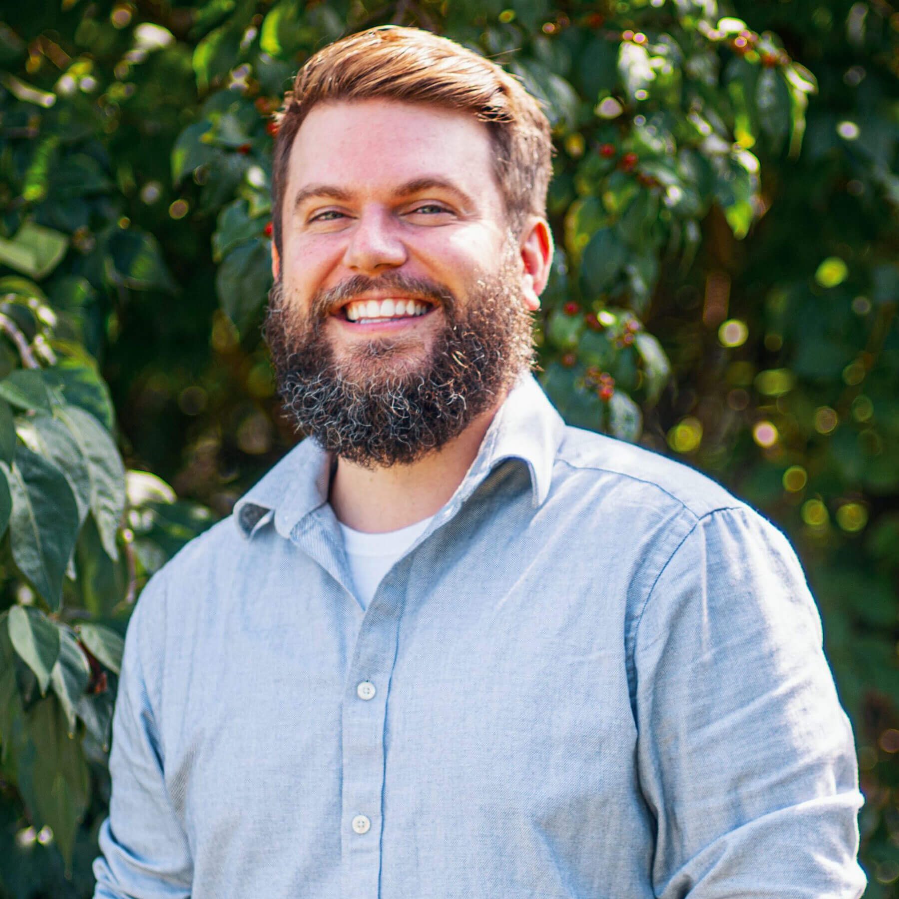 Bearded, brunette man smiling with trees in the background