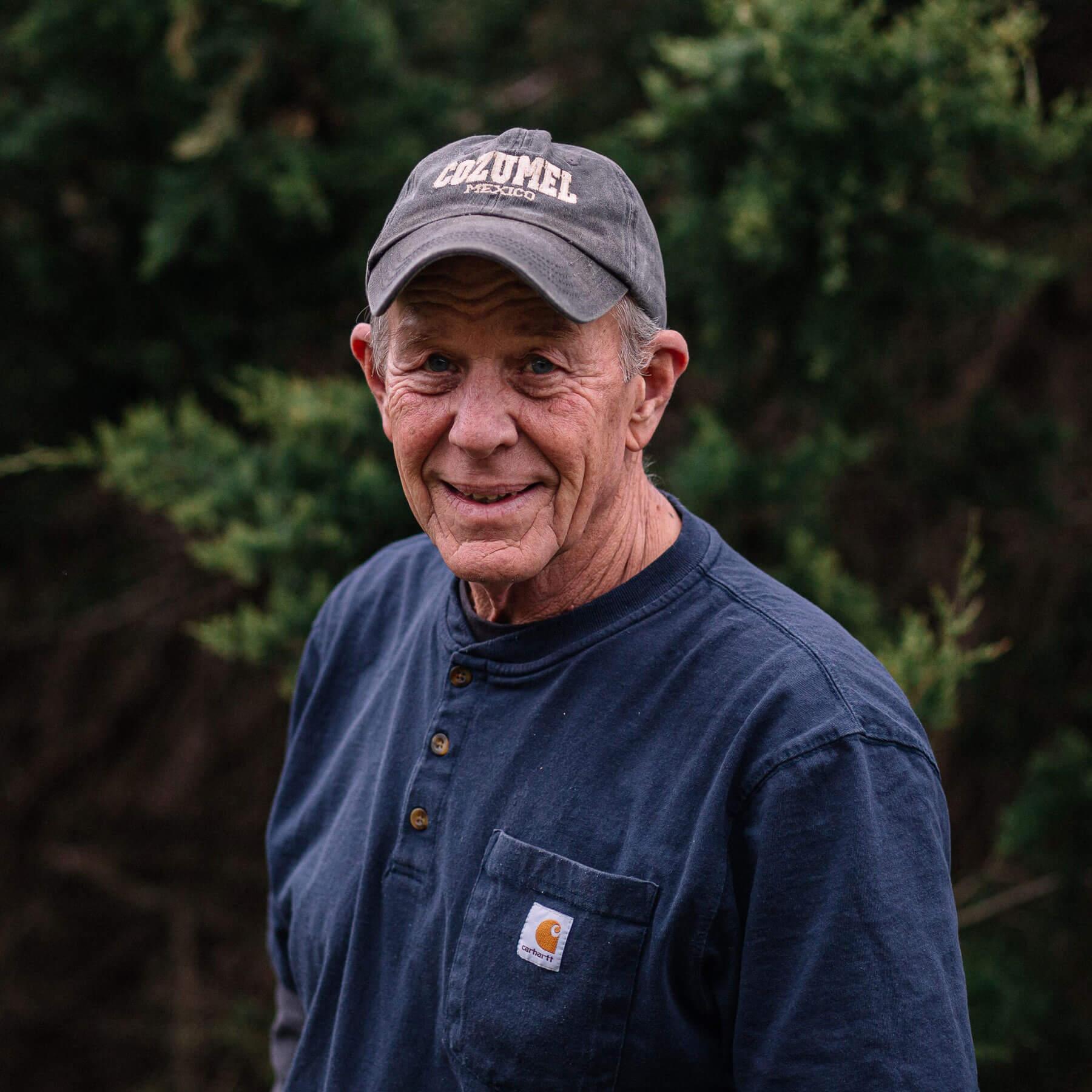 Man smiling for camera with a hat on and trees in the background