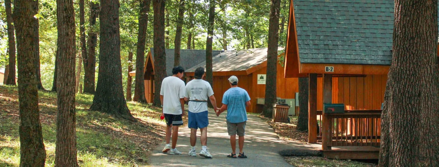 Campers walking on a path amid cabins, trees, and shadows