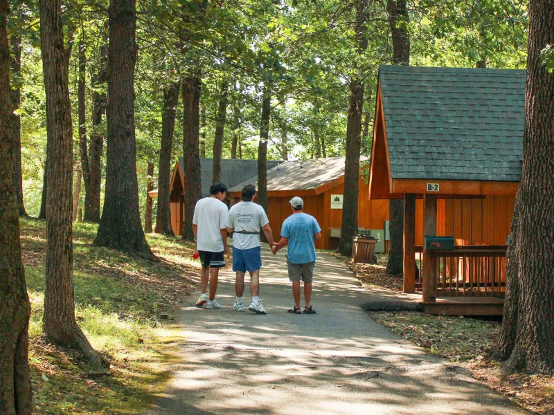 Campers walking on a path amid cabins, trees, and shadows
